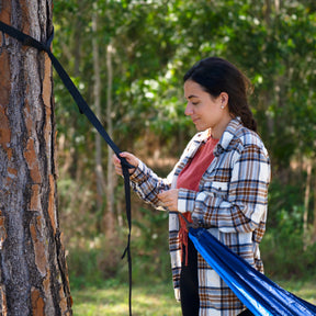 Woman securing the Bliss 54-inch Wide camping hammock to a tree strap that is wrapped around a tree.