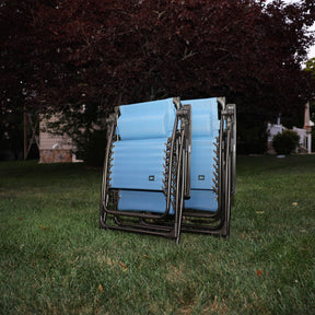 Set of 2 26-inch denim blue Zero Gravity Chairs folded on a lawn.