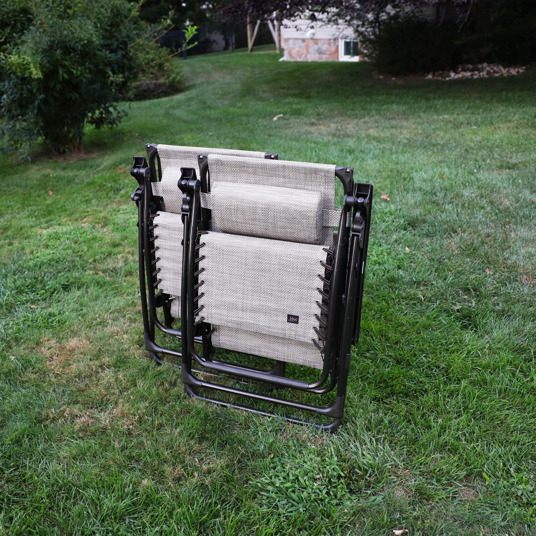 Set of 2 26-inch sand Zero Gravity Chairs folded on a lawn.