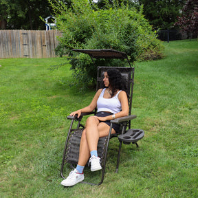 Girl sitting in the 26-inch Brown Jacquard Zero Gravity Chair on a lawn with the canopy positioned above her.