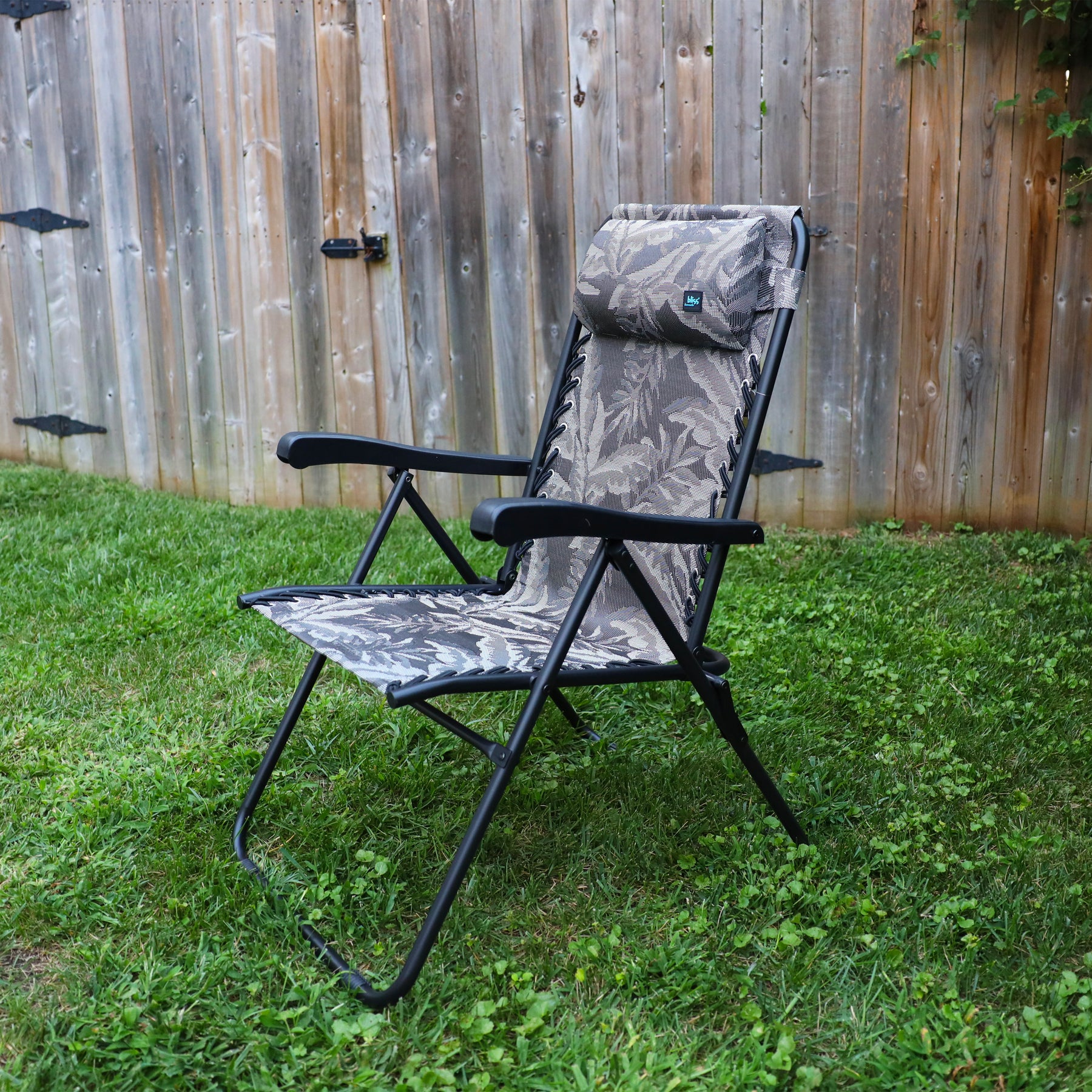 26-inch Reclining Platinum fern Sling Chair on a lawn next to a fence.