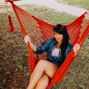 Woman relaxing in the orange Bliss Hammocks 40-inch Island Rope Hammock Chair outside.