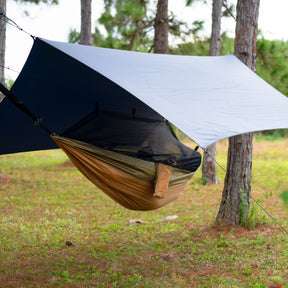 Person relaxing outside in a hammock underneath the Bliss Hammocks Rain Shelter.