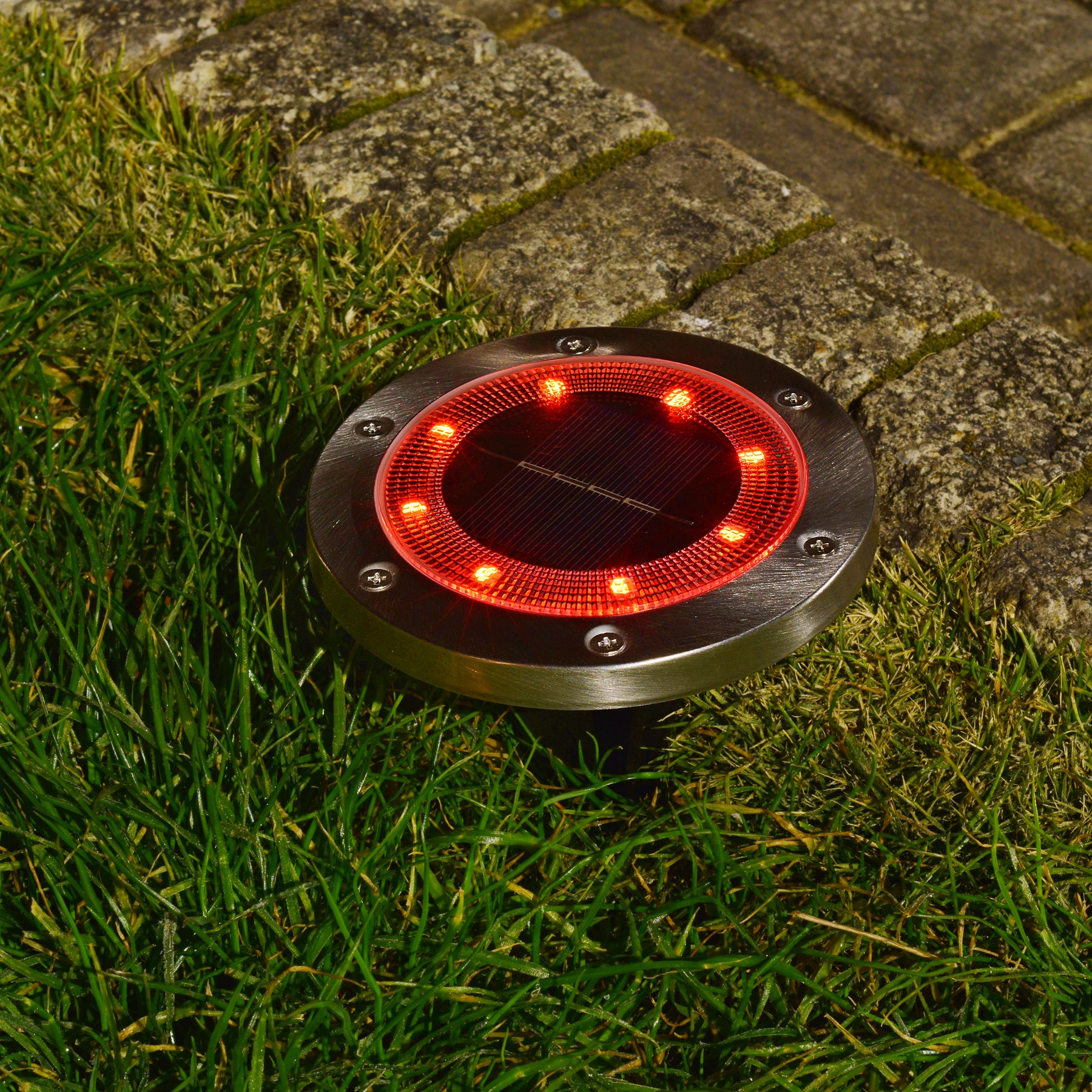 Bliss Outdoors Solar Powered LED Metal Disc Pathway light in the ground lighting up red.