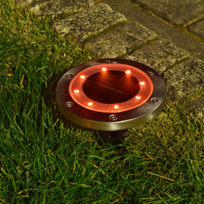 Bliss Outdoors Solar Powered LED Metal Disc Pathway light in the ground lighting up orange.