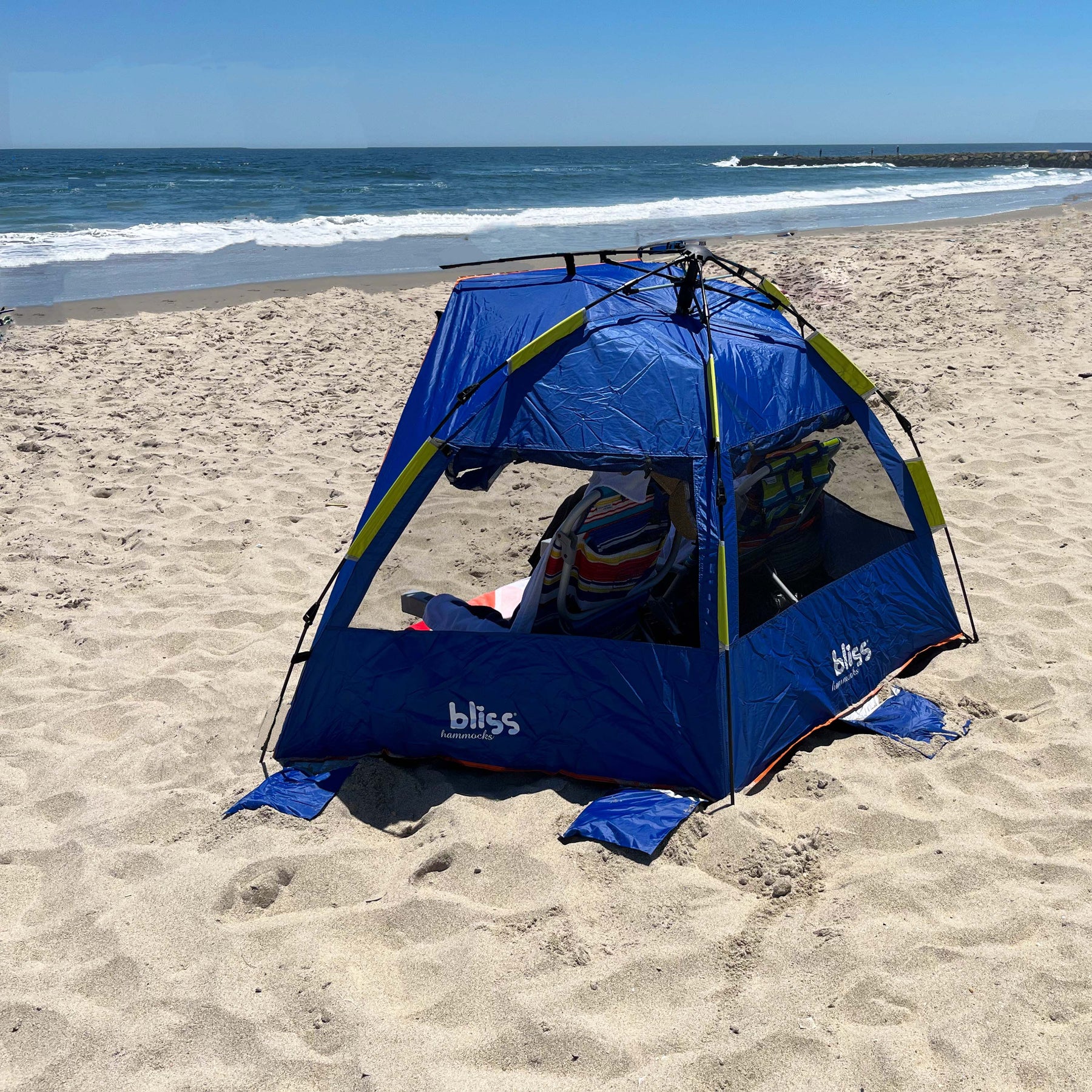 Bliss Hammocks Pop-Up Beach Tent with a collapsible design assembled on the beach with chairs inside and the ocean in the background.