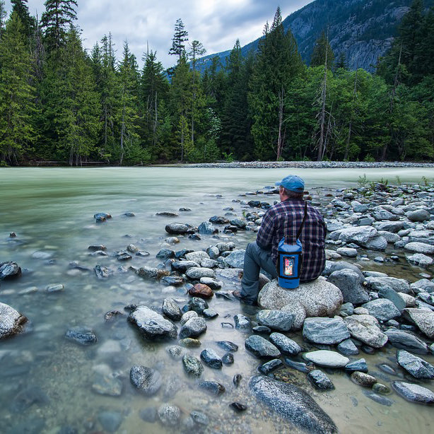 Man sitting on a rock next to a river wearing the TrailGear 20 liter Dry Bag Back Pack with netted pockets.