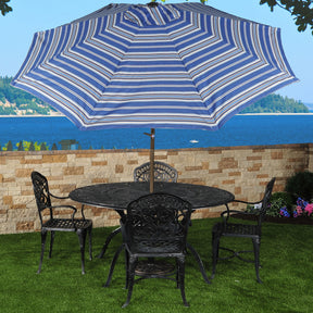 Patio set of umbrella, chairs, and table set up in a backyard with the ocean in the background.