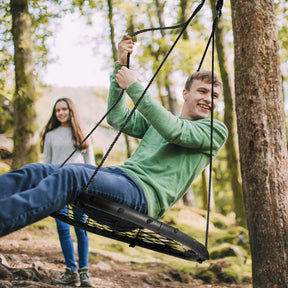 Boy swinging from a tree on the Bliss Outdoors Rope Tree Glider with Hanging Kit. A girl in the background is watching him have fun.